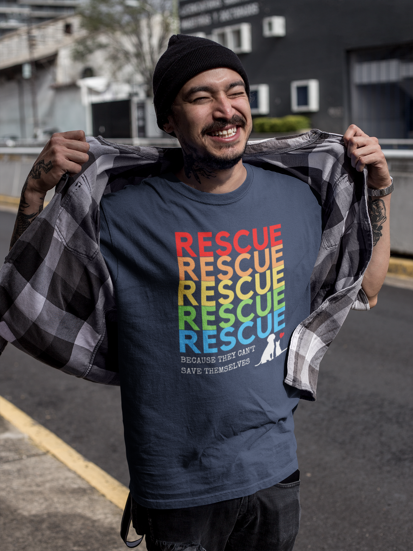 Navy Blue Tshirt “Rescue – Because They Can’t Save Themselves” rainbow animal rescue shirt, standing outdoors in the city. This colorful cat and dog rescue T-shirt promotes TNR, fostering, and animal rescue awareness — perfect for volunteers and compassionate pet lovers.