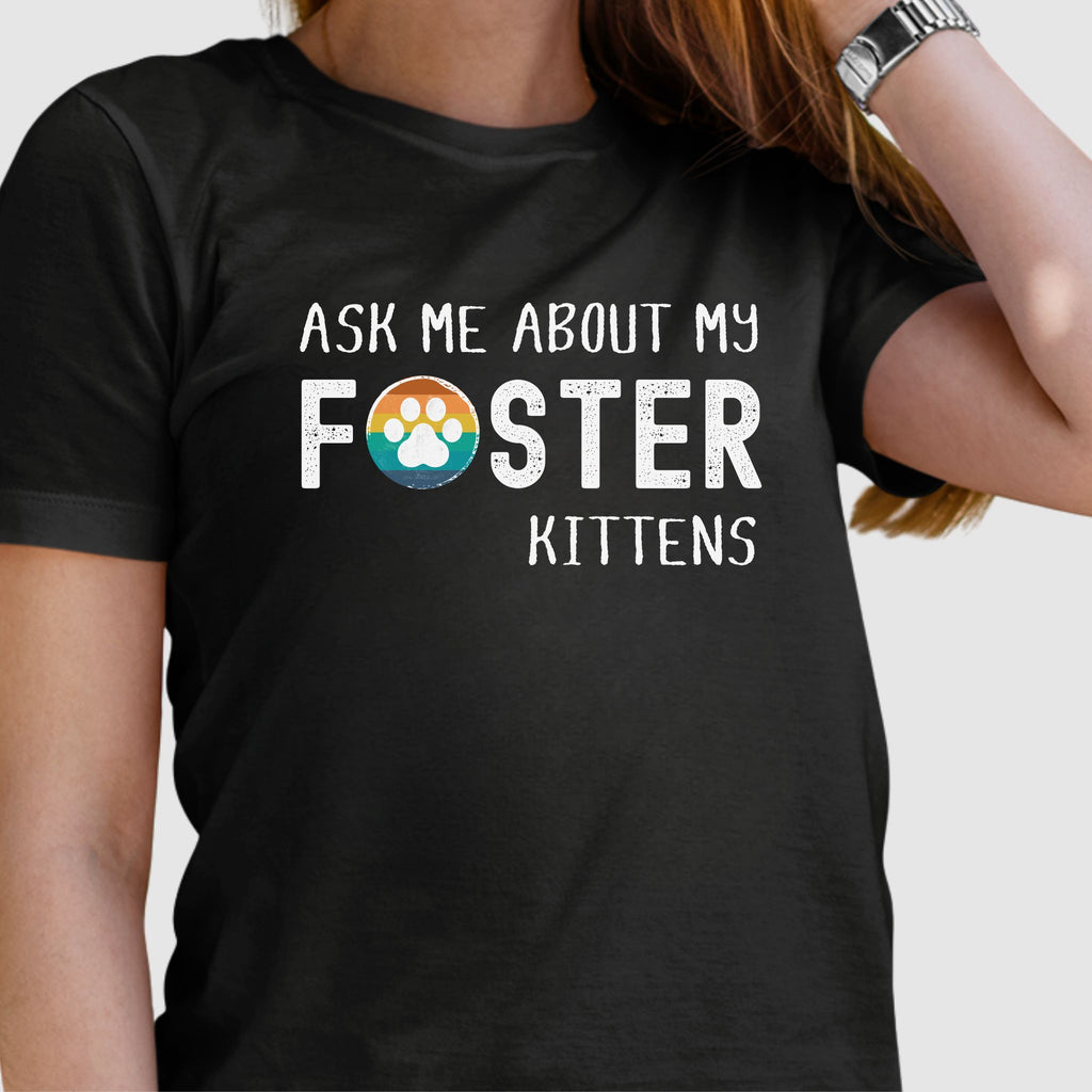Black soft t-shirt with text that reads ‘Ask Me About My Foster Kittens’ and a rainbow paw-print graphic in the word Foster