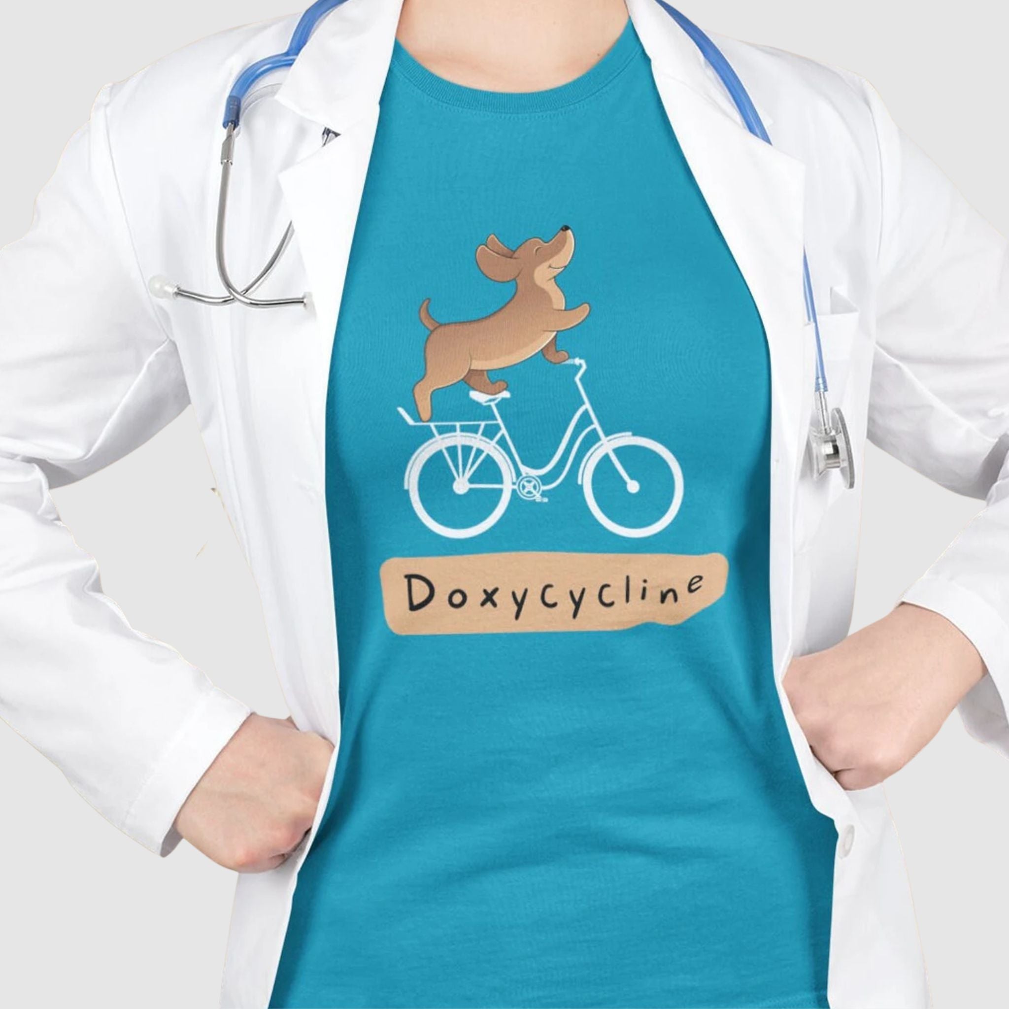 Veterinarian Vet Tech Spay Neuter Staff wearing a lab coat and stethoscope over a turquoise t-shirt with a cartoon dog riding a bicycle and the word ‘Doxycycline.’ Cute vet-med pun shirt