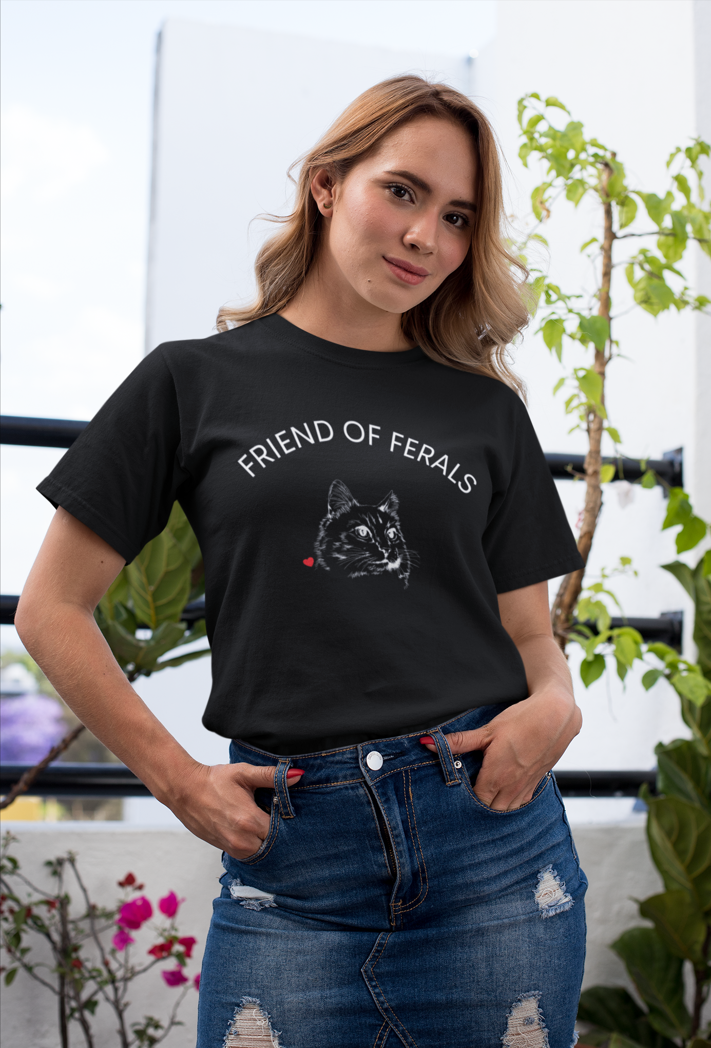 A man wearing a black “Friend of Ferals” TNR awareness shirt featuring a detailed cat illustration and red heart, standing outdoors in the woods. This feral cat rescue shirt supports animal rescue, TNR, and community cat advocates — perfect gift for cat lovers and volunteers.