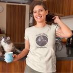 Person in kitchen wearing a t-shirt with 'Foster Mama Saving Tiny Lives' design featuring a kitten and person holding tabby foster kitten.