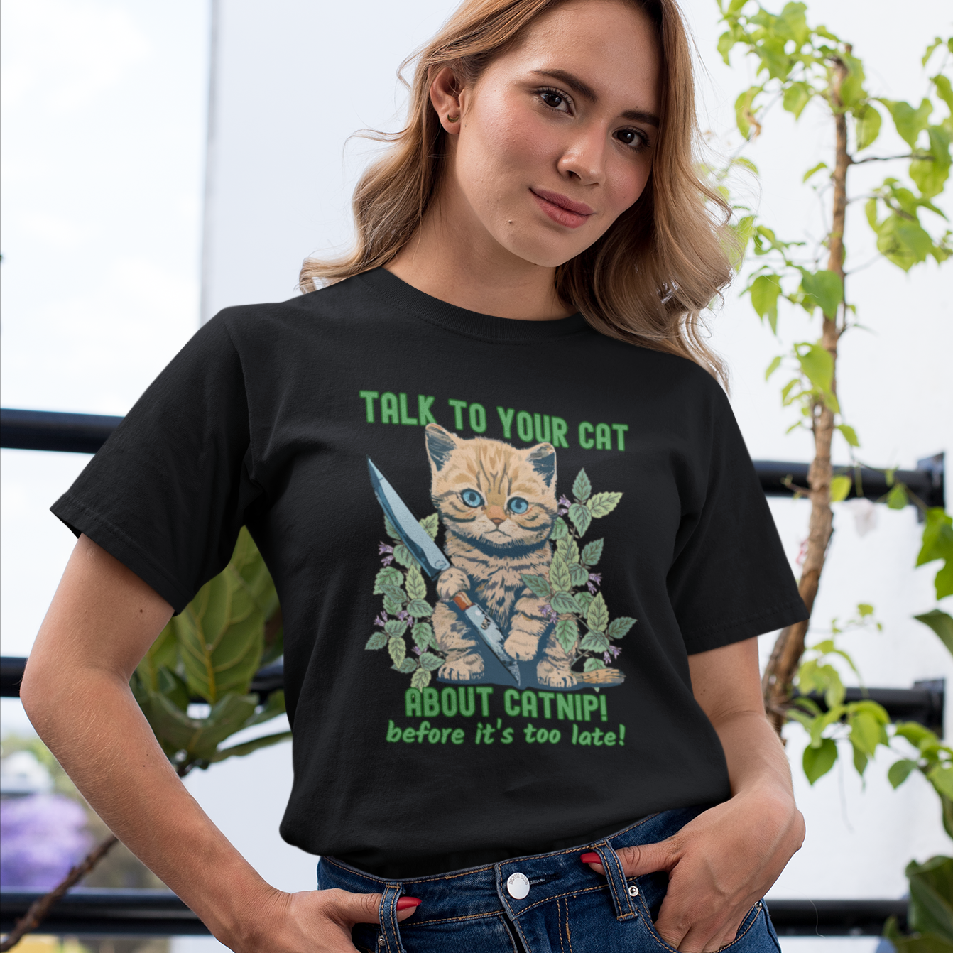 Woman wearing at-shirt with a cute kitten holding a knife surrounded by catnip leaves and the text ‘Talk to Your Cat About Catnip Before It’s Too Late.’ Funny cat lover shirt.