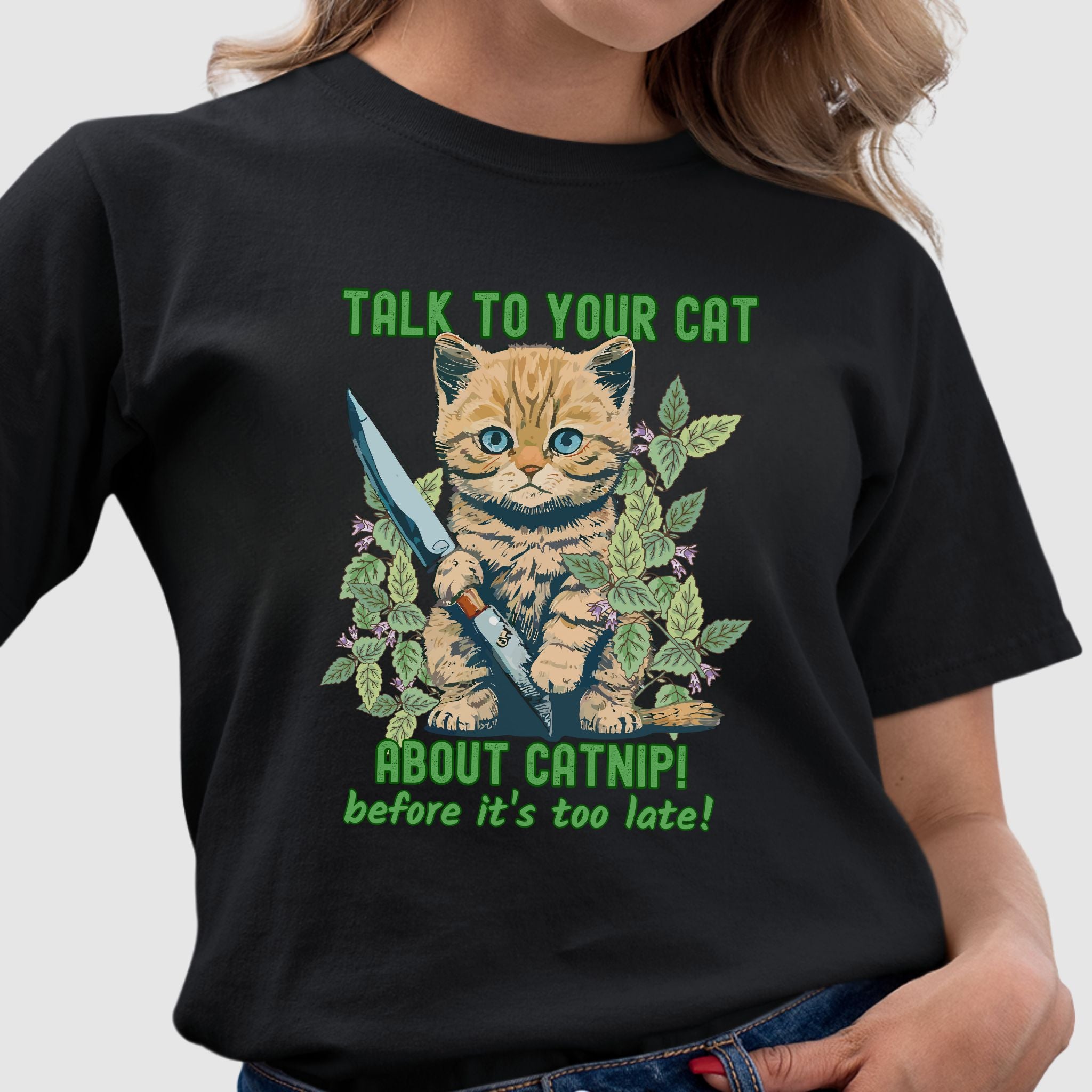 Model wearing a black t-shirt with a cute kitten holding a knife surrounded by catnip leaves and the text ‘Talk to Your Cat About Catnip Before It’s Too Late.’ Funny cat lover shirt.