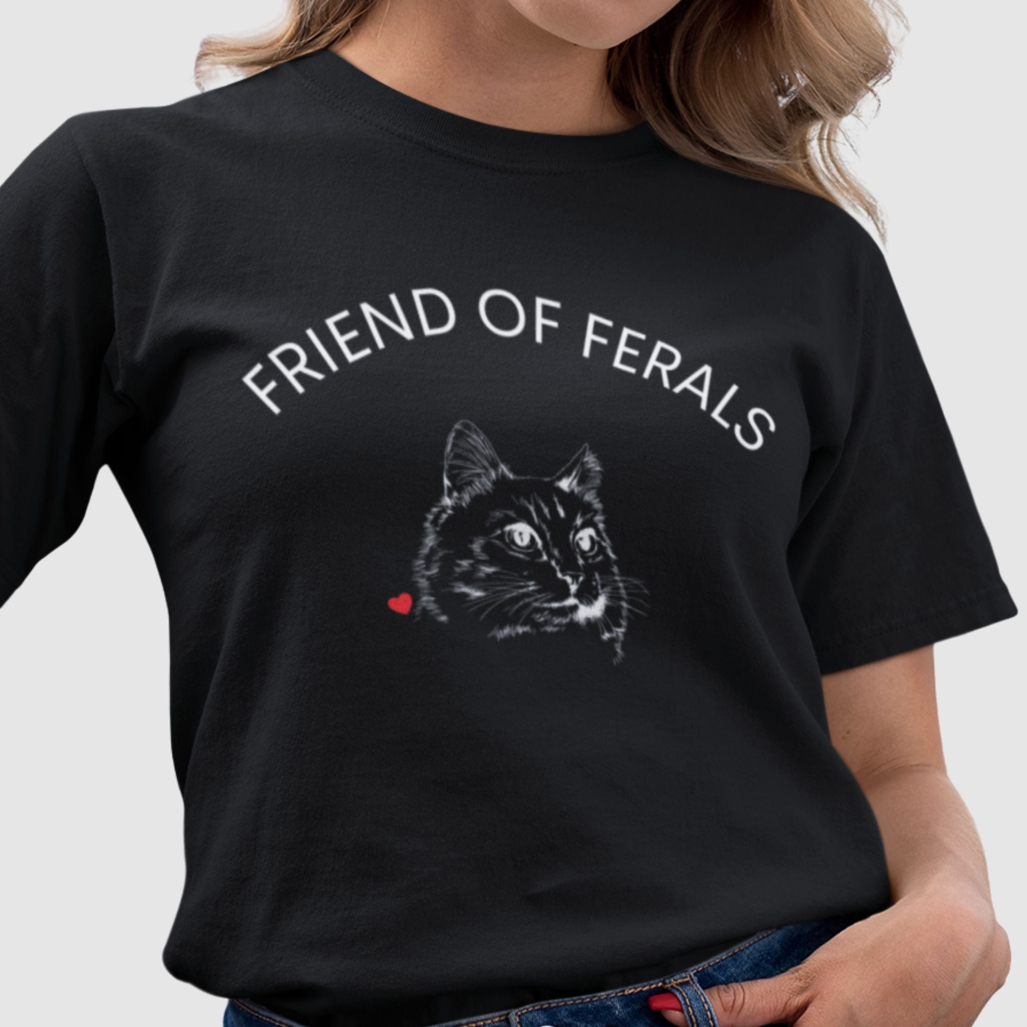 woman wearing a black tshirt with bold text reading friend of ferals minimalist design of a cat with line art expressive eyes and ear tip showing that stray cat has been TNR Trap Neuter Return small read heart
